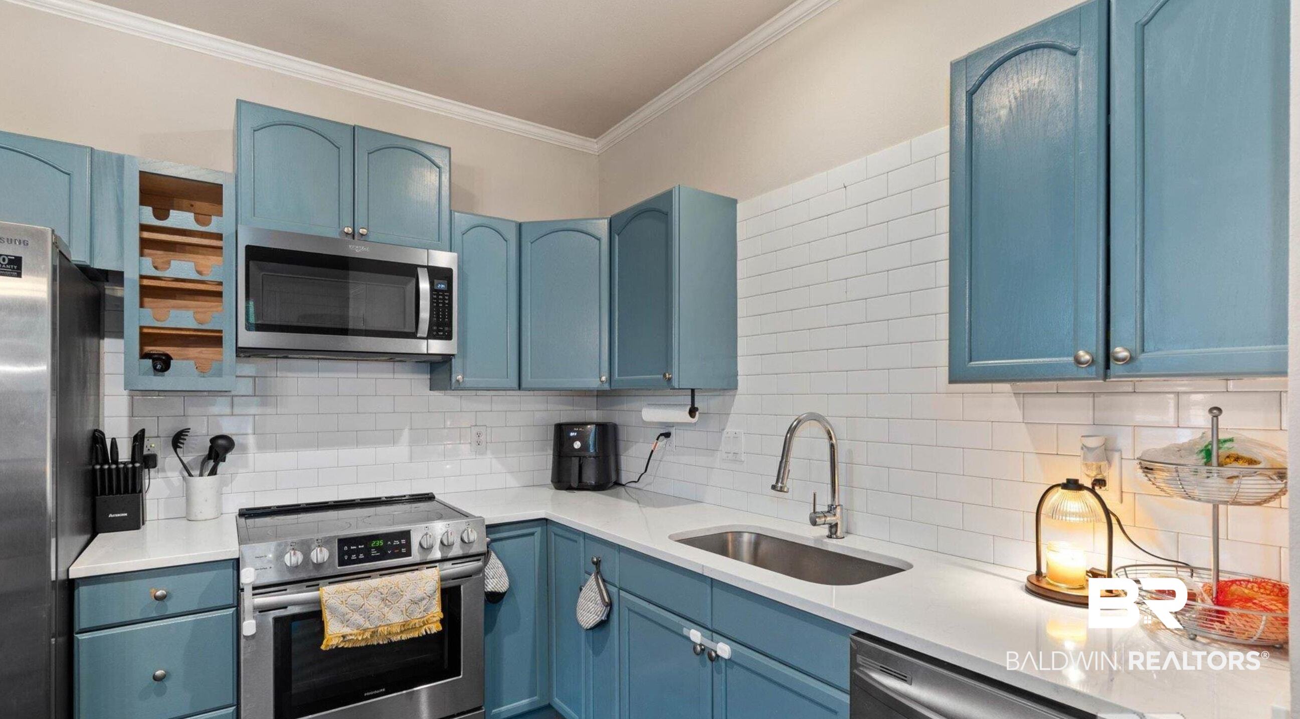 25806 Pollard Road, Unit 203 Daphne, AL 36526 - Photo 5 of 14 Kitchen with blue cabinetry, stainless steel appliances, ornamental molding, tasteful backsplash, and light stone counters