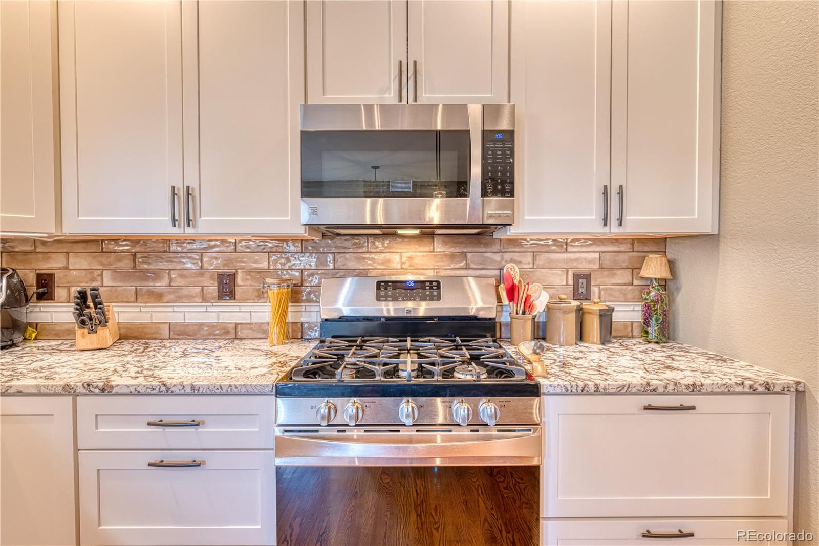 6378 Umber Circle Arvada, CO 80403 - Photo 24 of 50 a kitchen with granite countertop a stove a sink and white cabinets