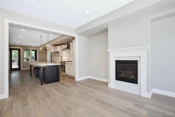 a living room with stainless steel appliances kitchen island granite countertop a refrigerator a stove and a wooden floors