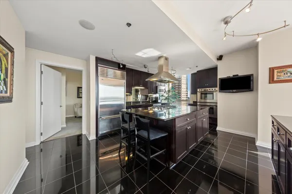 a living room with stainless steel appliances kitchen island granite countertop a table chairs and a refrigerator