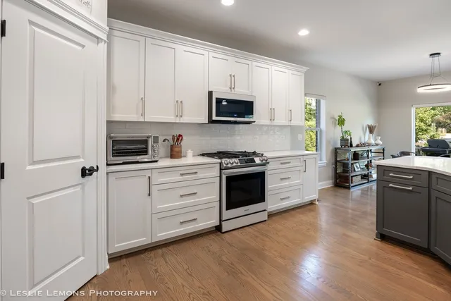 a kitchen with stainless steel appliances granite countertop white cabinets a sink a stove a refrigerator and microwave with wooden floor