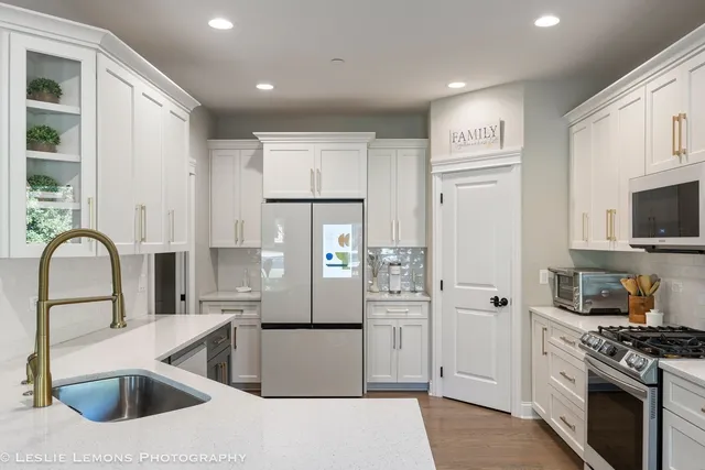 a kitchen with stainless steel appliances kitchen island granite countertop a refrigerator oven a sink dishwasher and white cabinets with wooden floor