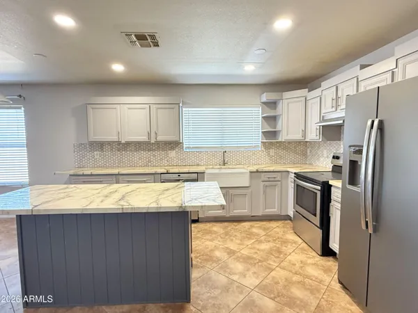a kitchen with granite countertop a refrigerator a sink and white cabinets