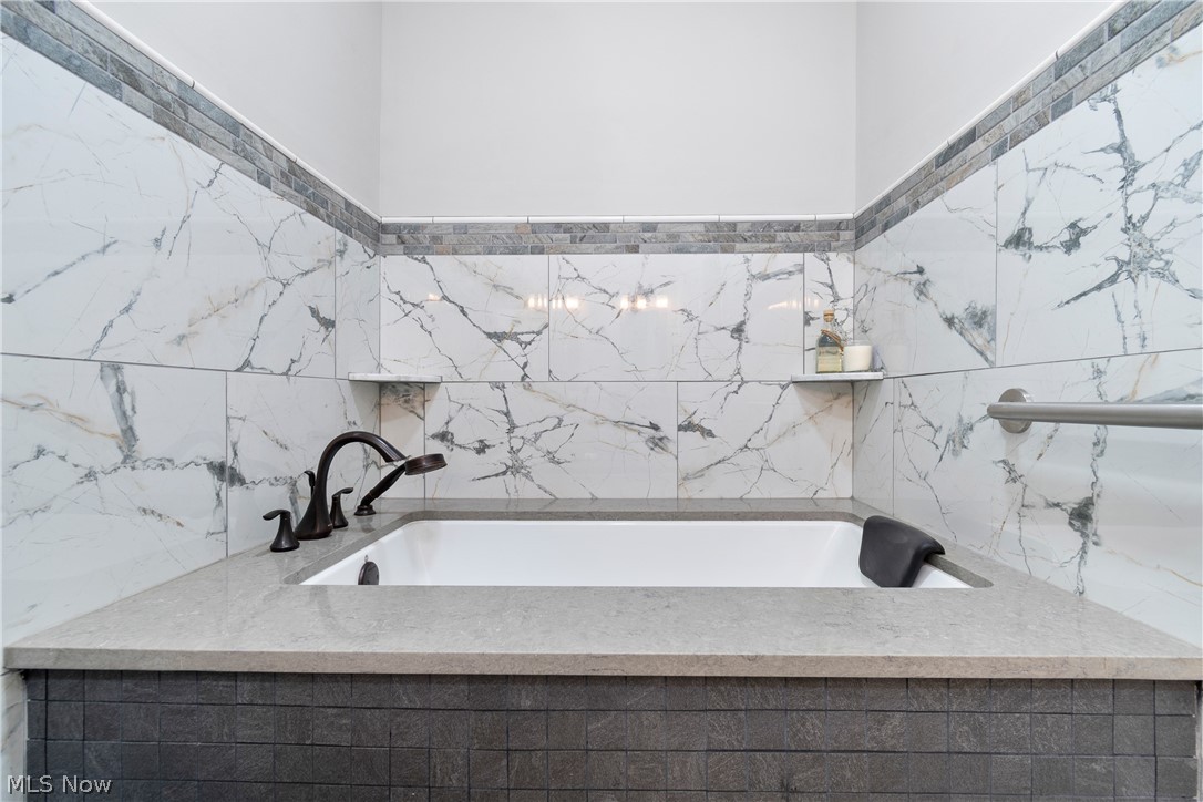 443 Merriman Road Akron, OH 44303 - Photo 22 of 44 Built-in bathtub featuring a dark bronze faucet, a light gray countertop, and white large-format wall tiles with gray veining
