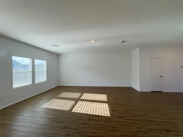 a view of an empty room with wooden floor and window