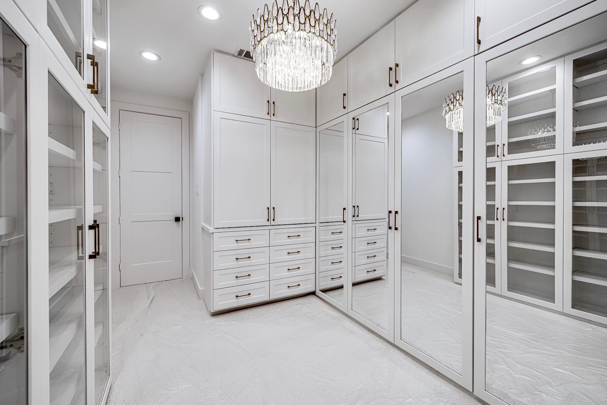 2411 Hazard Street Houston, TX 77019 - Photo 29 of 46 Additional view of the walk-in closet highlighting built-in shelving, sleek glass-front cabinets, and a stunning crystal chandelier that elevates the overall design. This closet provides both function and elegance with extensive storage options.