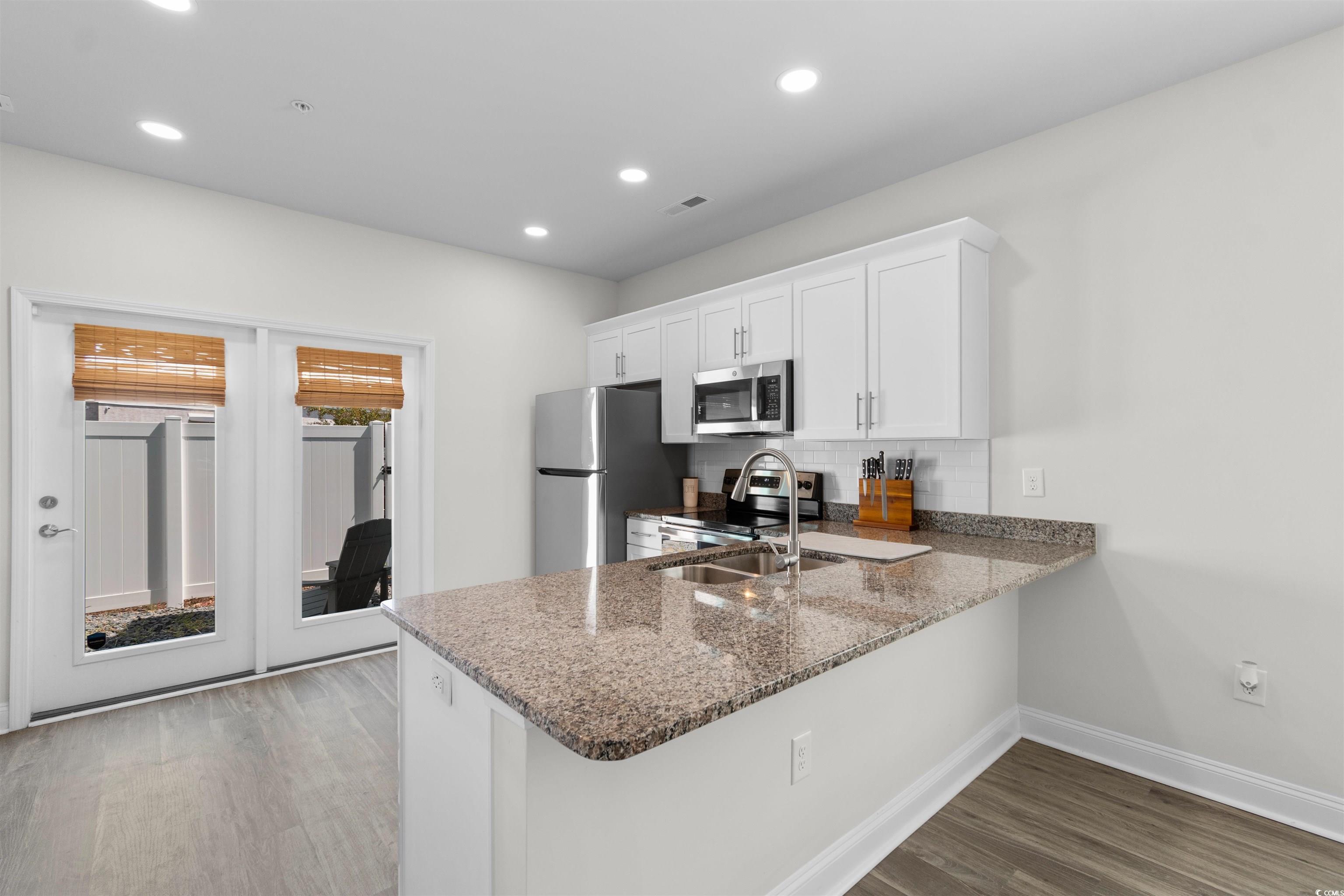 804 Moen Place, Unit F Myrtle Beach, SC 29577 - Photo 9 of 34 Kitchen featuring white cabinets, a peninsula, dark wood-style flooring, dark stone countertops, and backsplash