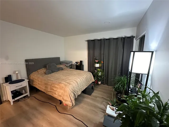 a bedroom with a bed potted plant on dresser and a wooden floor