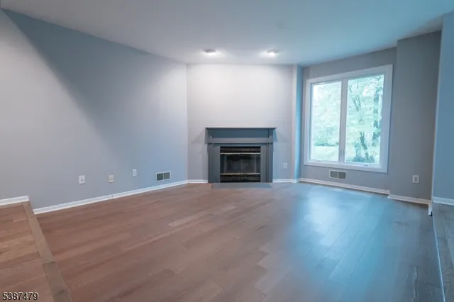 an empty room with wooden floor fireplace and windows