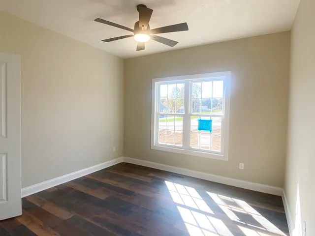 an empty room with wooden floor ceiling fan and windows