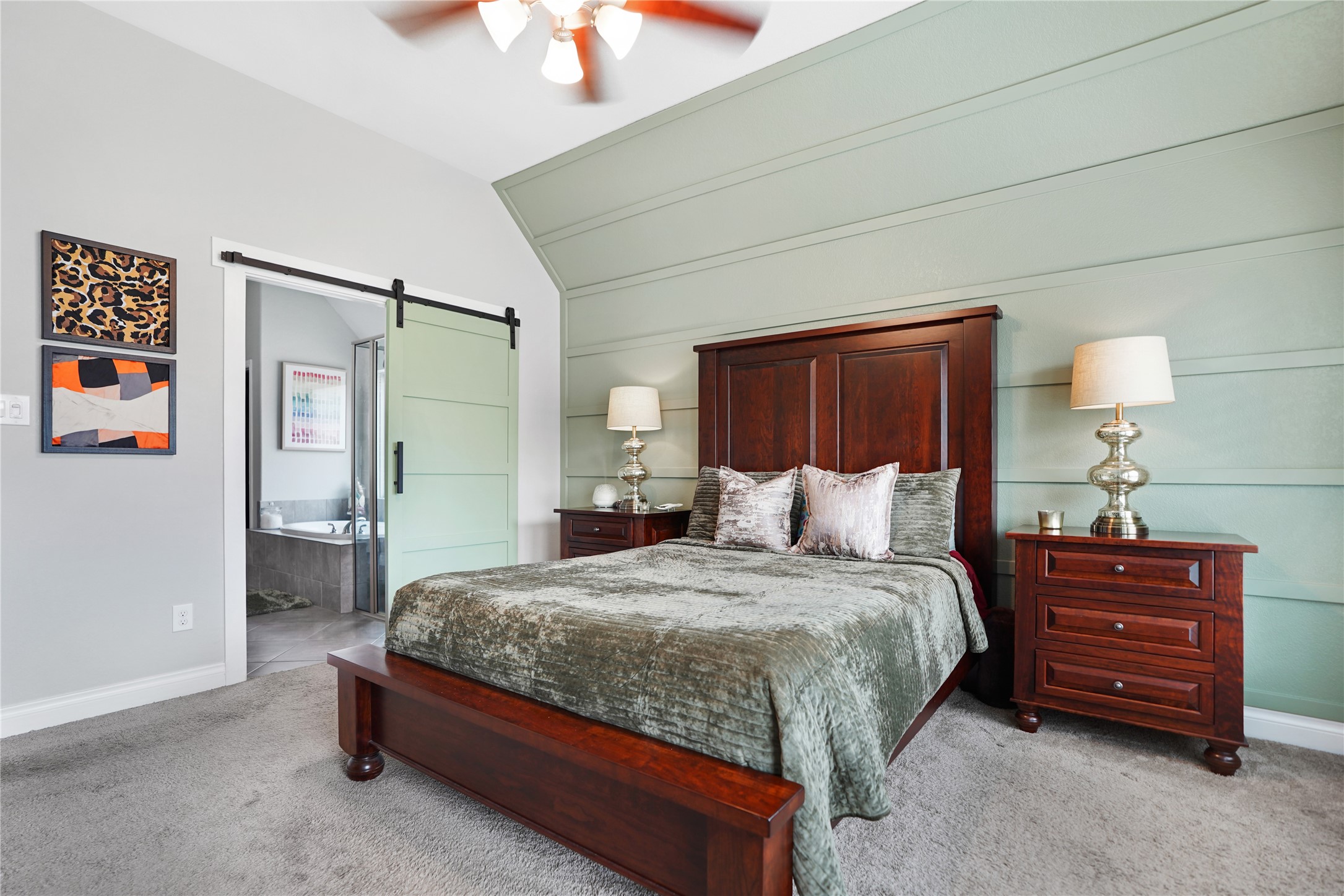 2345 Redwood Ridge Trail Manvel, TX 77578 - Photo 26 of 39 This bedroom features a modern design with a soft green accent wall and stylish wooden furniture, including a bed and matching nightstands. It has cozy carpeting, a ceiling fan, and a sliding barn door leading to an en-suite bathroom, creating a warm and inviting atmosphere.