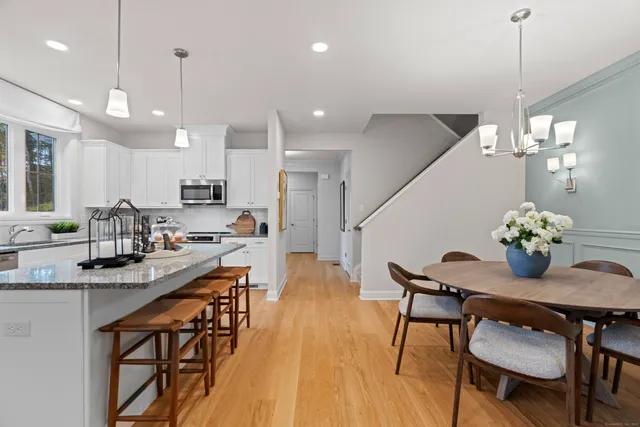 a kitchen with stainless steel appliances kitchen island granite countertop a dining table chairs stove and white cabinets with wooden floor