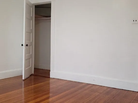 a view of an empty room with wooden floor and closet
