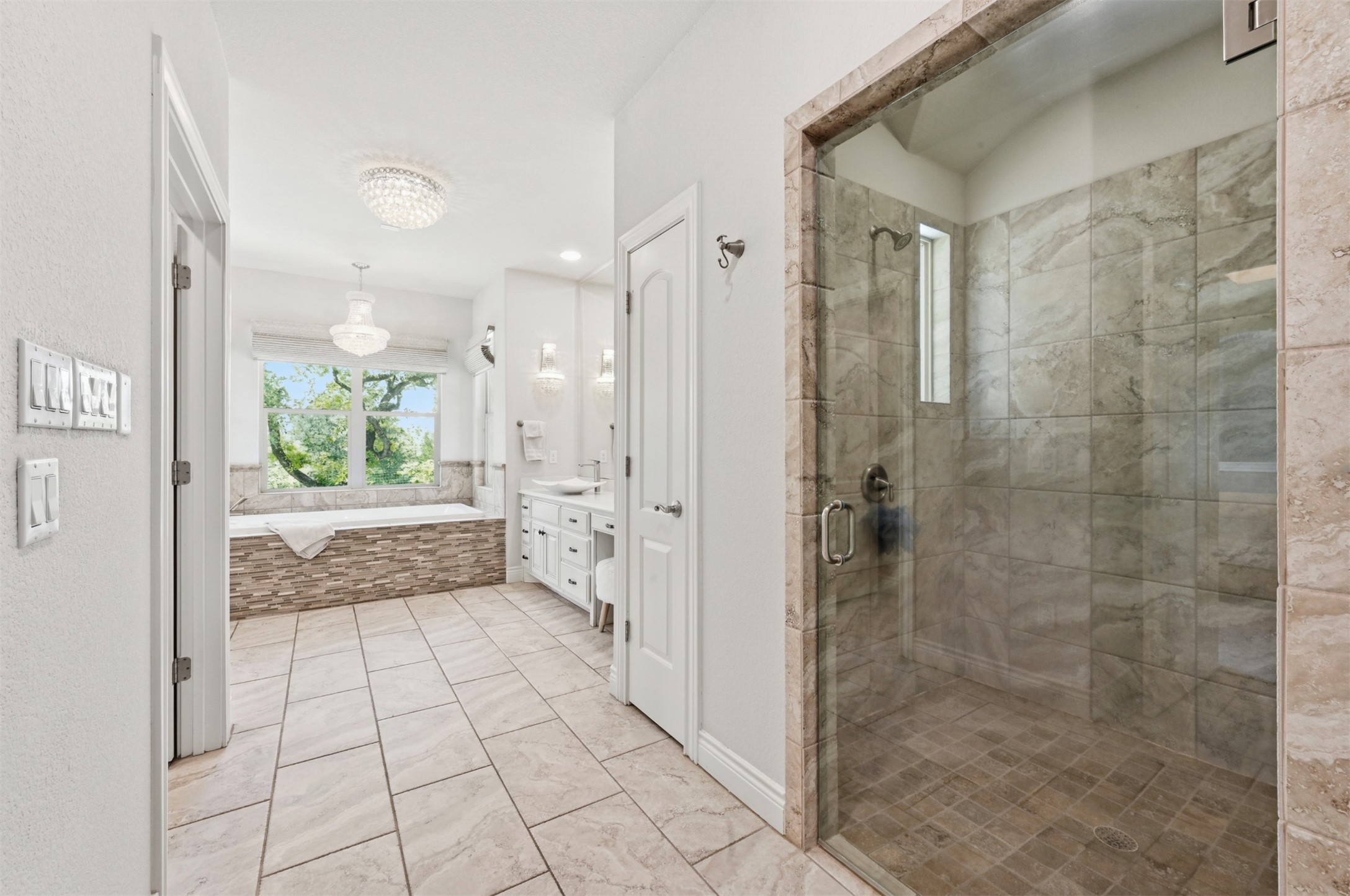 387 Corral Road Smithville, TX 78957 - Photo 17 of 40 Spacious bathroom featuring a frameless glass shower enclosure with tile surround, a built-in soaking tub with stone-finish paneling, dual vanity with undermount sinks, and large format tile flooring