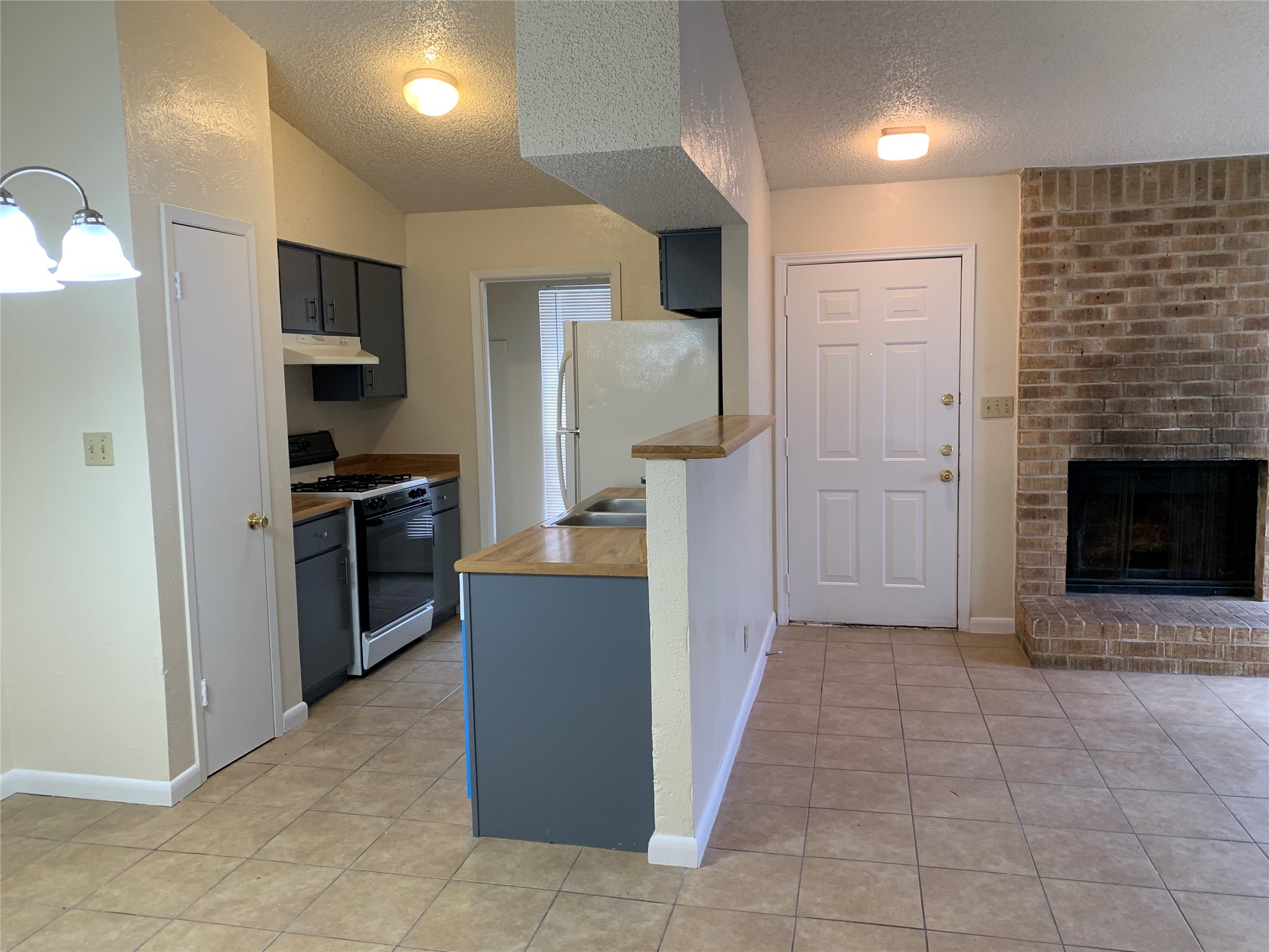 10447 Doc Holliday Trail, Unit B Austin, TX 78753 - Photo 15 of 19 Kitchen with range with gas cooktop, a textured ceiling, freestanding refrigerator, a brick fireplace, and light tile patterned floors