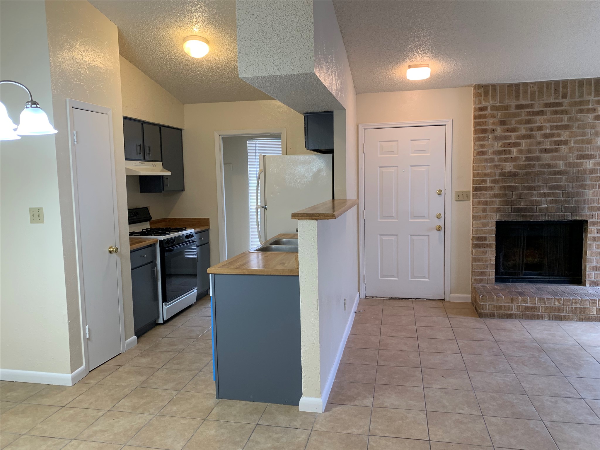10447 Doc Holliday Trail, Unit B Austin, TX 78753 - Photo 3 of 19 Kitchen with gas stove, a textured ceiling, freestanding refrigerator, light tile patterned floors, and a brick fireplace