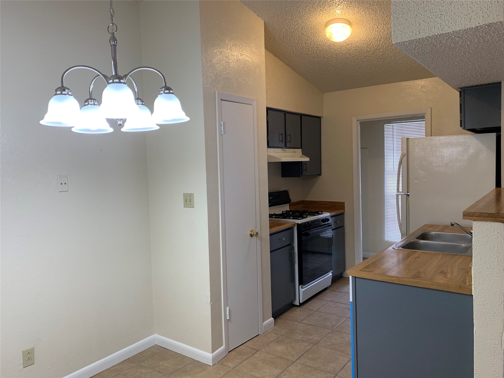 10447 Doc Holliday Trail, Unit B Austin, TX 78753 - Photo 4 of 19 Kitchen featuring range with gas cooktop, freestanding refrigerator, a chandelier, light tile patterned floors, and a textured wall