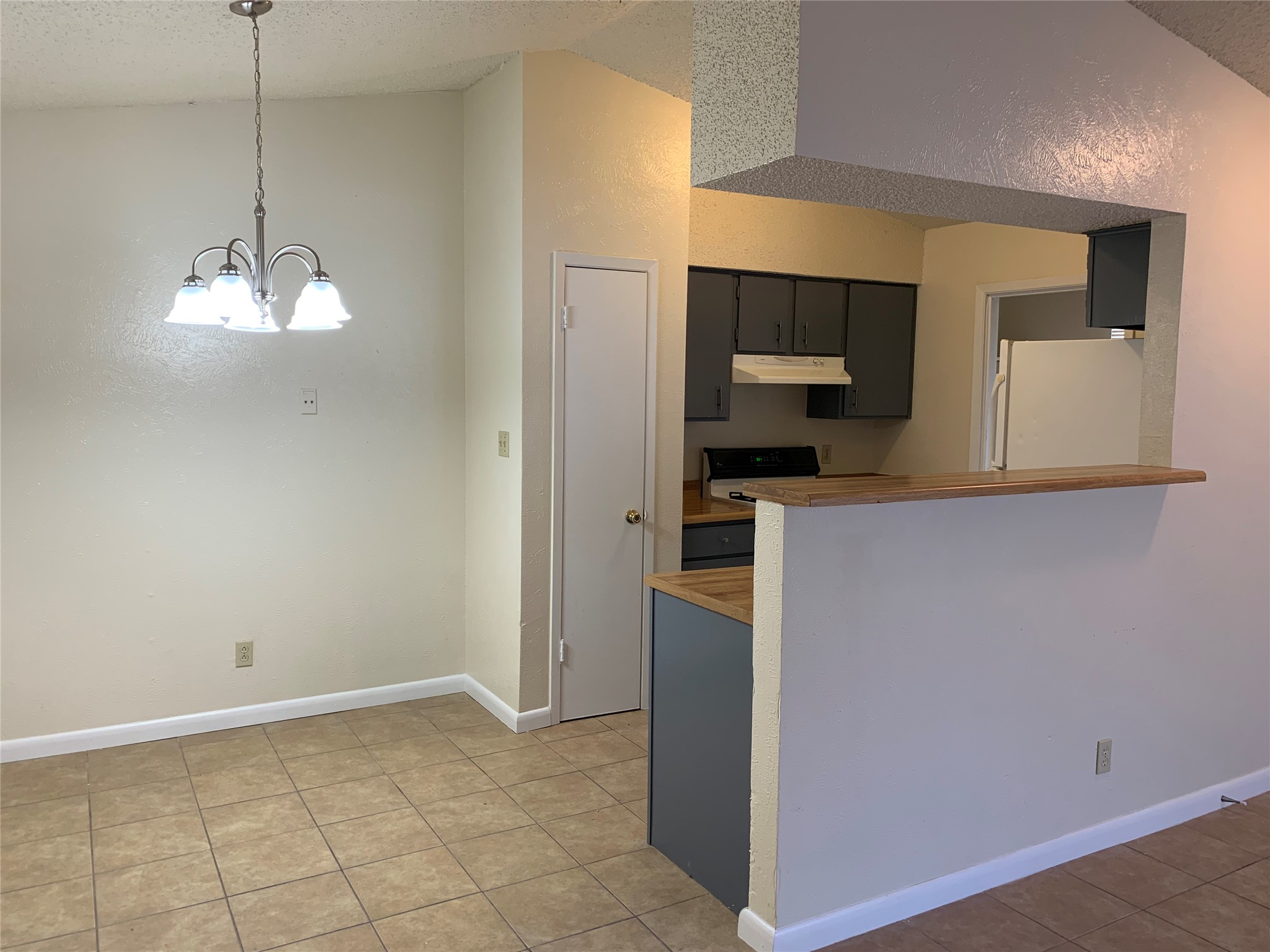 10447 Doc Holliday Trail, Unit B Austin, TX 78753 - Photo 6 of 19 Kitchen with freestanding refrigerator, a textured ceiling, suspended lighting, a peninsula, and light tile patterned floors