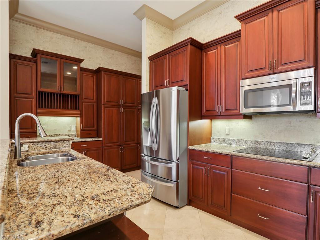 9241 Springview Loop Estero, FL 33928 - Photo 10 of 41 Kitchen featuring stainless steel appliances, light stone counters, wallpapered walls, glass insert cabinets, and crown molding
