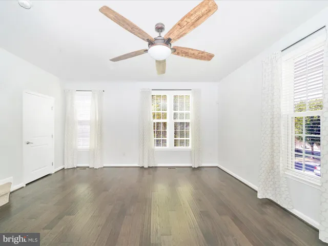 a view of an empty room with wooden floor and a ceiling fan