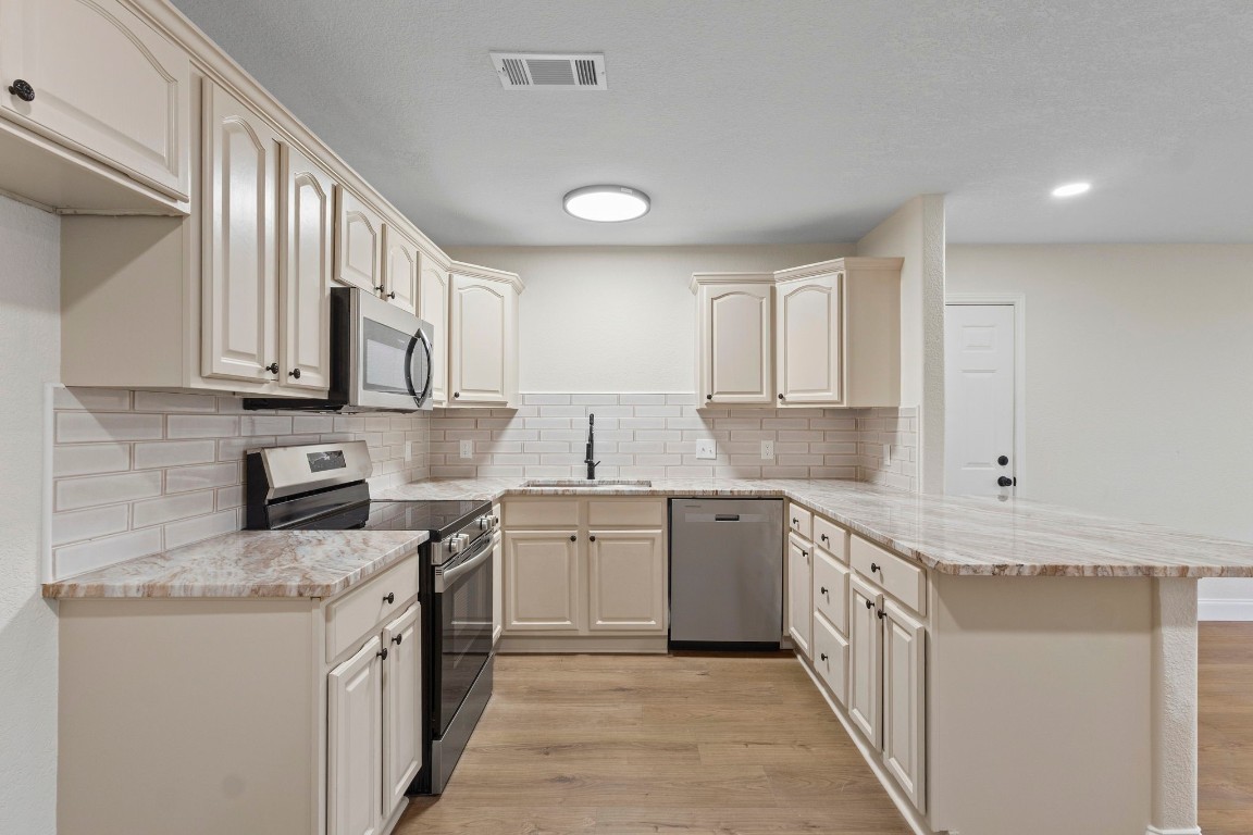 135 James Street Bridge City, TX 77611 - Photo 4 of 12 a kitchen with stainless steel appliances granite countertop a stove top oven a sink dishwasher and a refrigerator with wooden cabinets