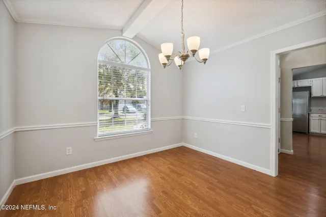 an empty room with wooden floor chandelier and a window