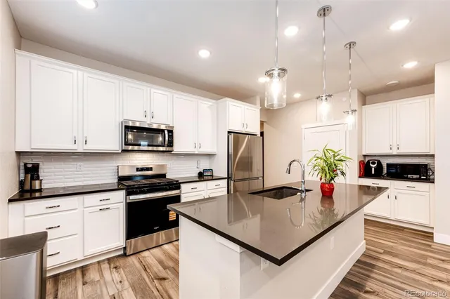 a kitchen with stainless steel appliances kitchen island granite countertop a stove a sink dishwasher a refrigerator and white cabinets with wooden floor