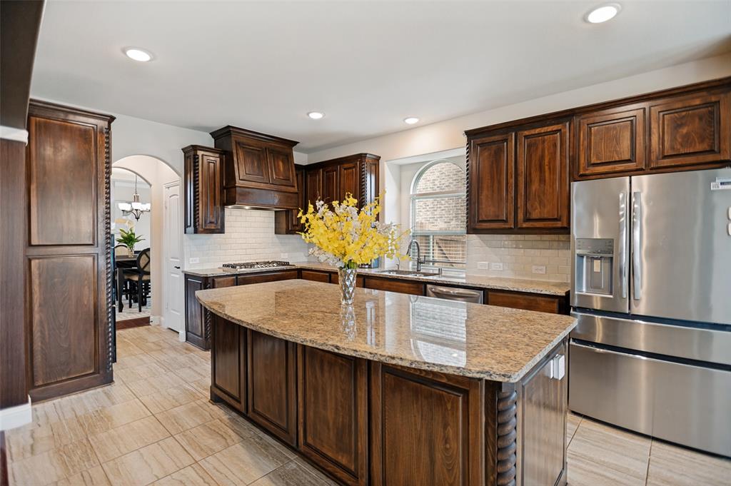 413 Frontier Court Midlothian, TX 76065 - Photo 9 of 26 Kitchen featuring dark wood cabinetry, a central island with a stone countertop, stainless steel appliances, a tile backsplash, and recessed lighting