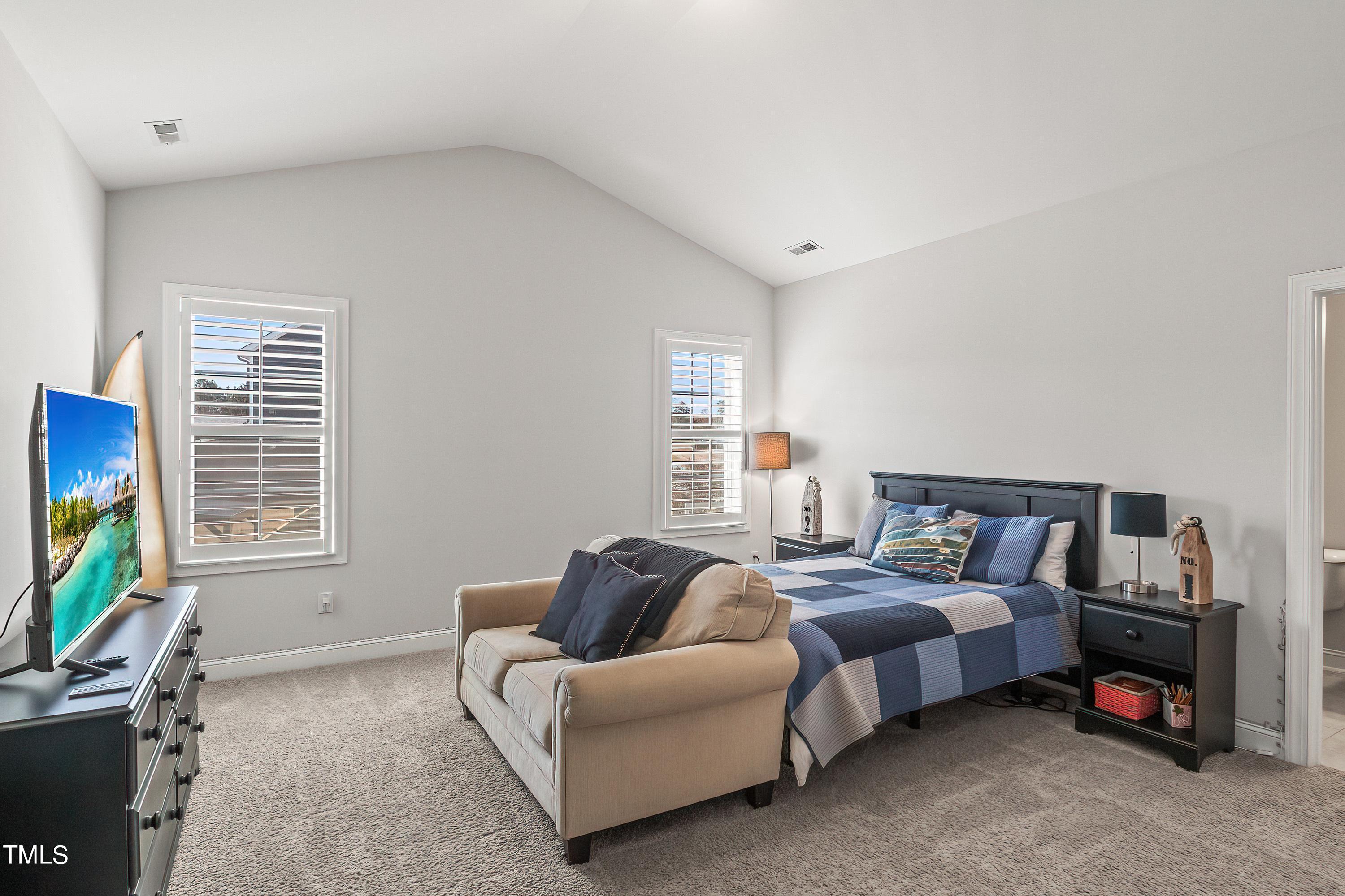 2025 Braeburn Drive Apex, NC 27539 - Photo 50 of 71 a spacious bedroom with a bed a couch and a flat tv screen on the dresser