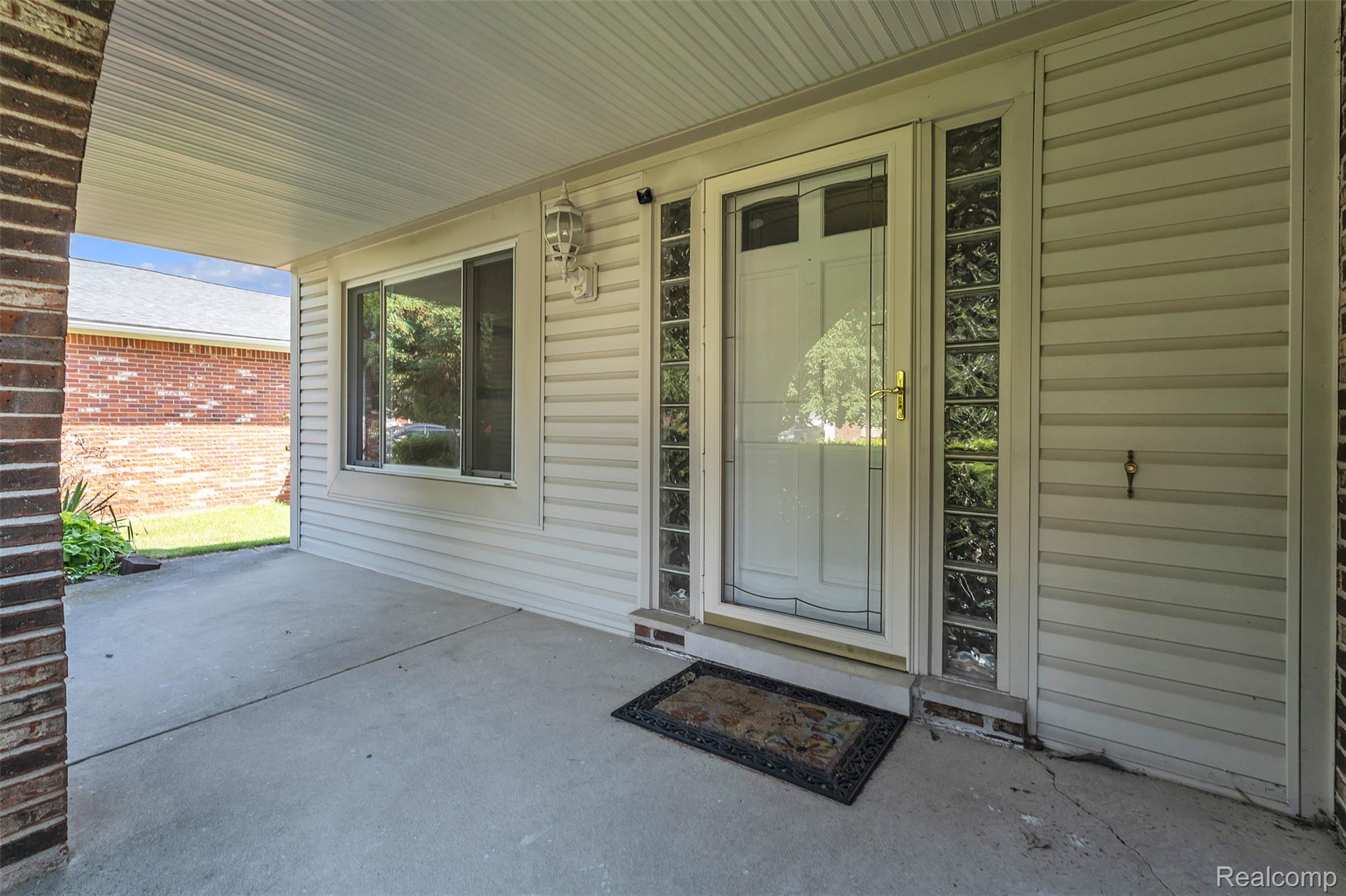 7000 Woonsocket Street Canton, MI 48187 - Photo 4 of 65 Covered concrete front porch featuring a white entry door with glass paneling, glass block sidelights, and a wall-mounted outdoor light fixture