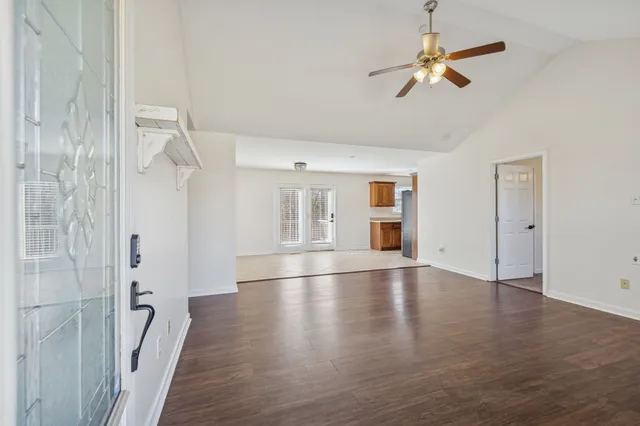 an empty room with wooden floor chandelier fan and windows