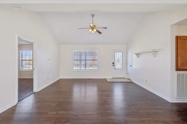 an empty room with wooden floor chandelier fan and windows