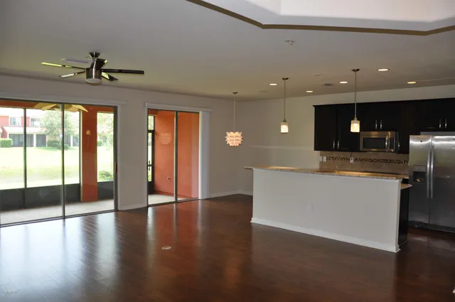 a view of an empty room with wooden floor and a kitchen