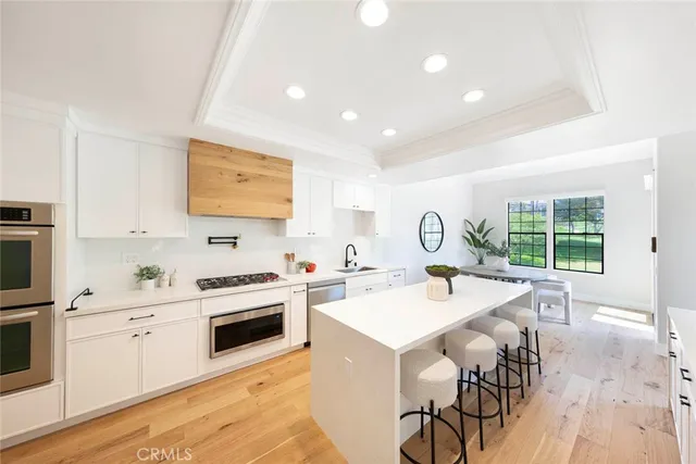 a open kitchen with stainless steel appliances granite countertop a stove top oven a sink a dining table and chairs with wooden floor