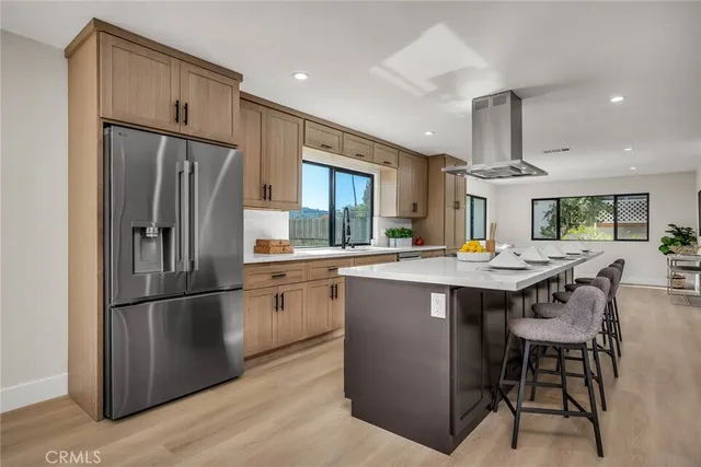 a kitchen with stainless steel appliances granite countertop a refrigerator a sink dishwasher a dining table and chairs with wooden floor