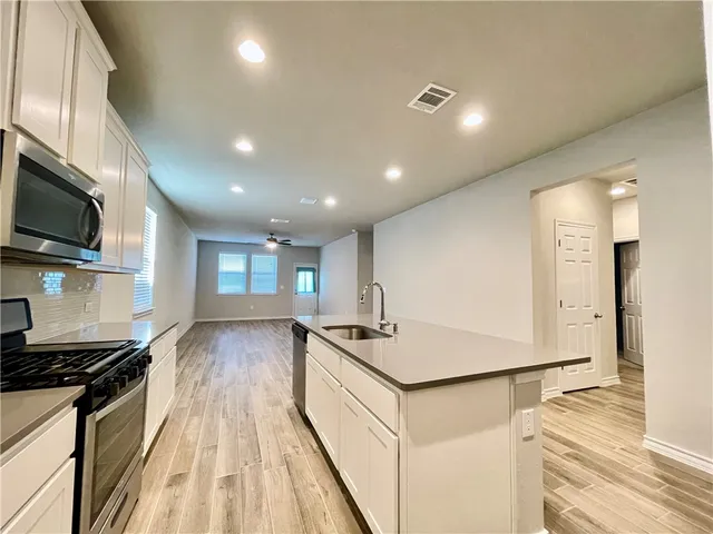 a view of a kitchen with kitchen island a sink wooden floor and stainless steel appliances