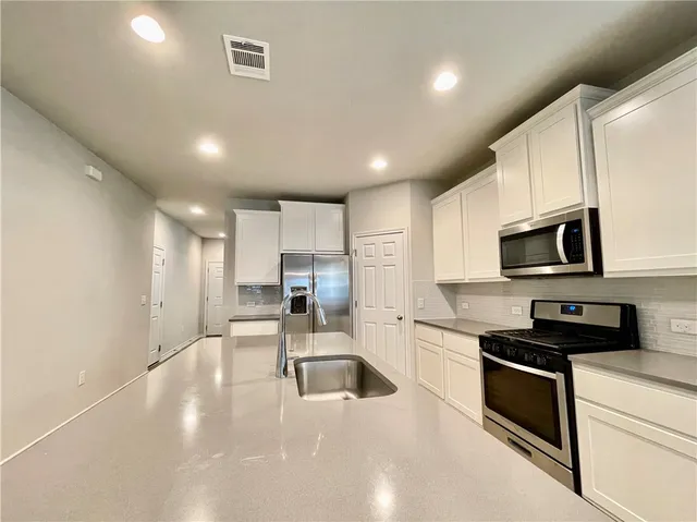 a kitchen with stainless steel appliances a stove a sink a refrigerator white cabinets and a refrigerator