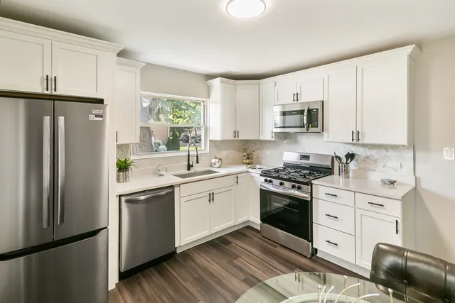 a kitchen with white cabinets white stainless steel appliances and window