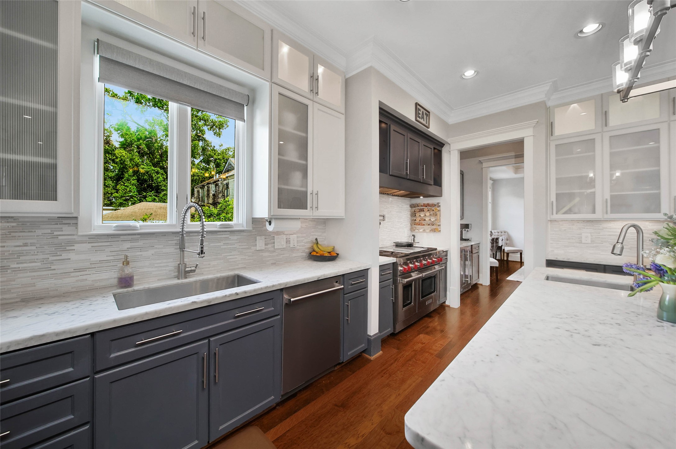 416 West 33rd Street Houston, TX 77018 - Photo 14 of 47 Thoughtfully designed with elevated finishes throughout, the kitchen features custom cabinetry accented by frosted reeded glass upper cabinets, adding texture and architectural interest. A large picture window above the oversized single-basin sink fills the space with natural light while offering serene backyard views, perfectly complementing the clean, sophisticated design aesthetic