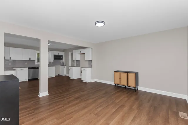 a view of empty room with wooden floor and kitchen