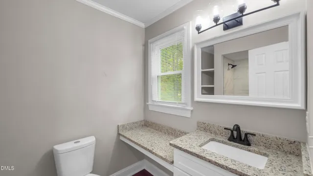 a bathroom with a granite countertop sink a toilet and a window