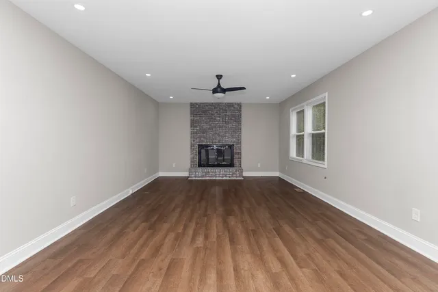a view of an empty room with wooden floor fireplace and a window