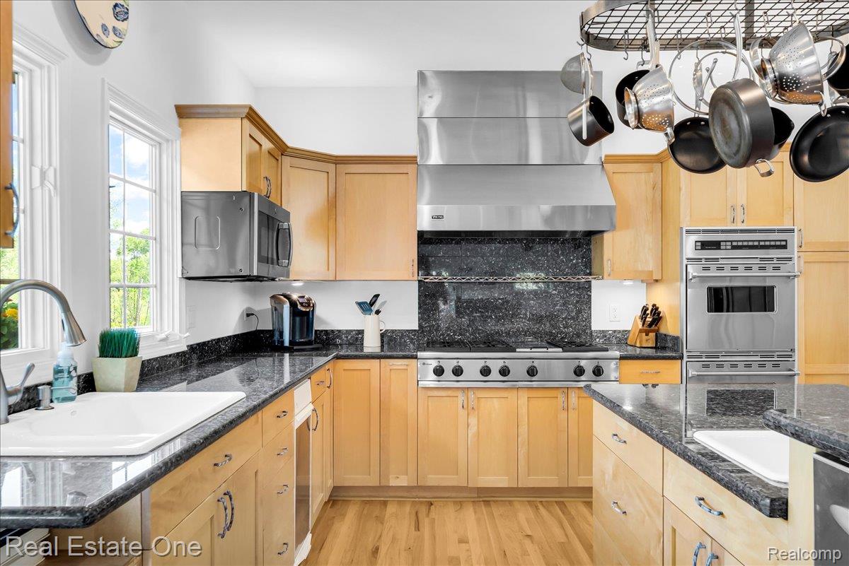 33850 Braebury Ridge Farmington, MI 48331 - Photo 17 of 85 Kitchen featuring natural wood cabinetry, dark granite countertops, stainless steel appliances, hardwood flooring, and a white undermount sink with a gooseneck faucet