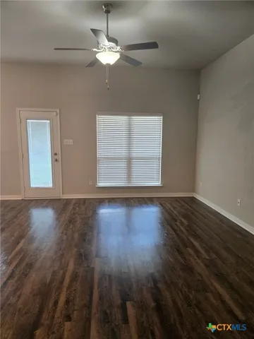 an empty room with wooden floor chandelier fan and windows