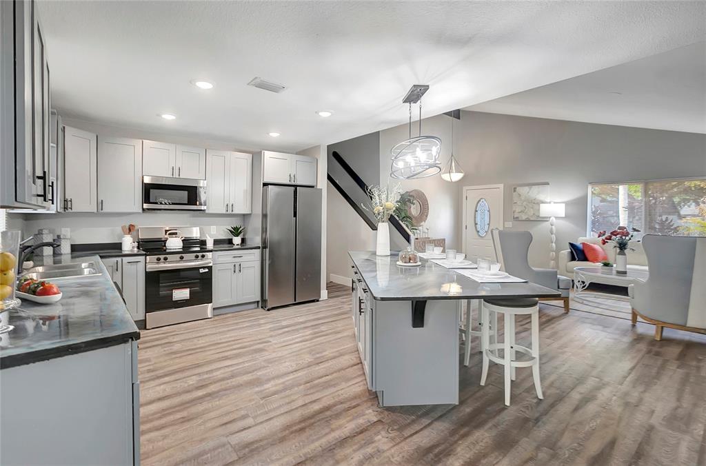 16133 Ravendale Drive Tampa, FL 33618 - Photo 14 of 46 a kitchen with stainless steel appliances kitchen island granite countertop a stove top oven a sink a dining table and chairs with wooden floor