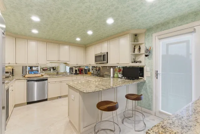 a kitchen with kitchen island granite countertop a stove a sink a refrigerator and white cabinets with wooden floor
