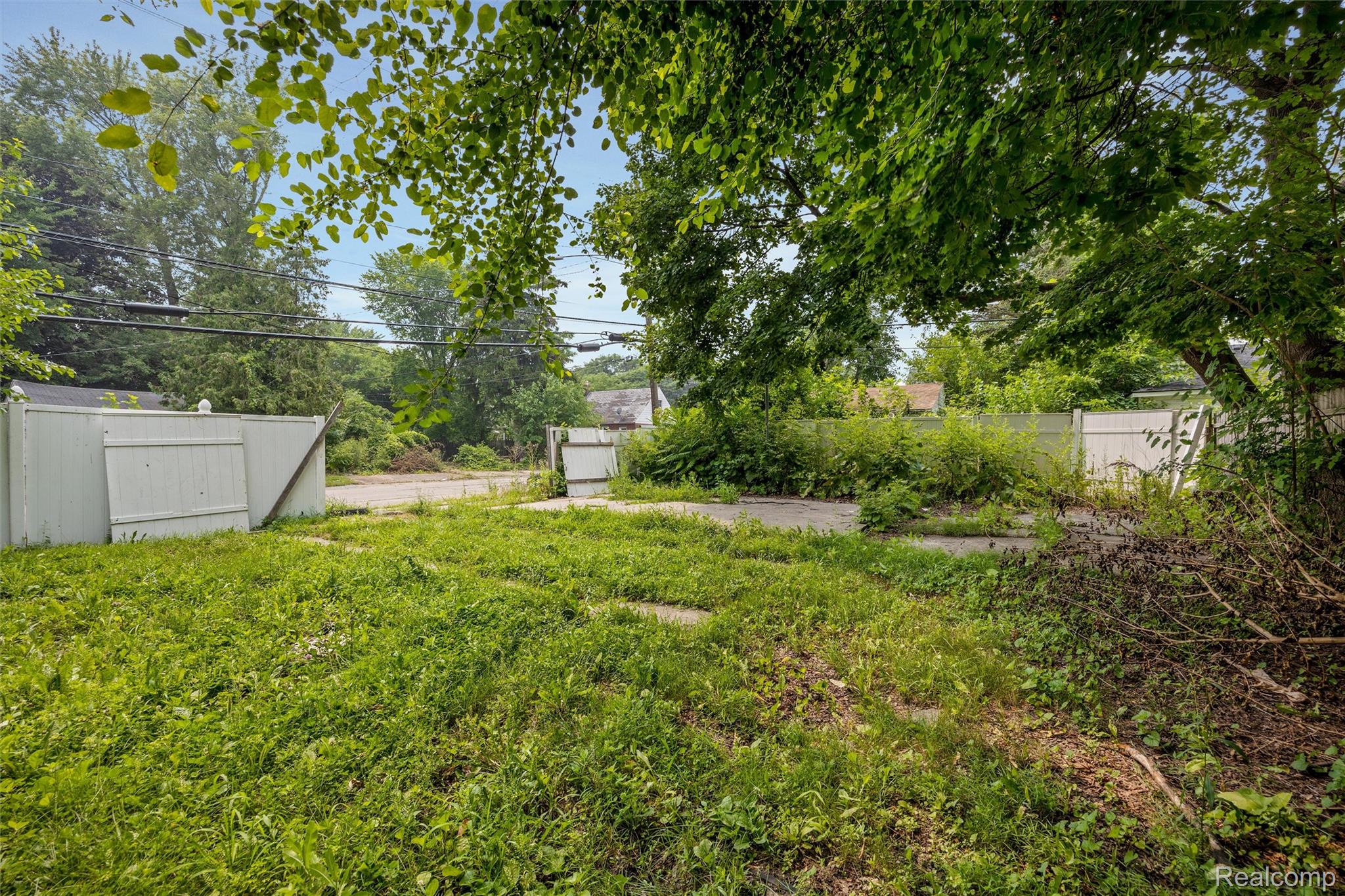 12603 Riad Street Detroit, MI 48224 - Photo 16 of 16 Expansive outdoor area featuring mature trees, a white perimeter fence, and direct paved access
