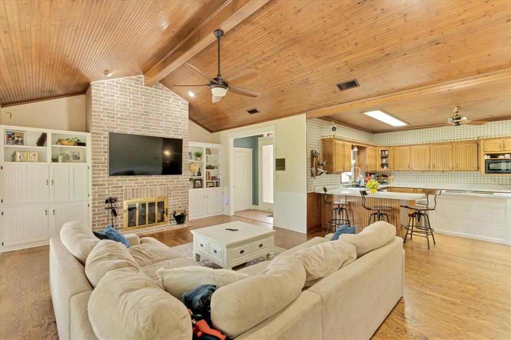 2717 Clear Lake Road Weatherford, TX 76087 - Photo 2 of 40 Spacious living area featuring a vaulted wood-plank ceiling, brick fireplace with a gold-tone screen, and built-in white cabinetry