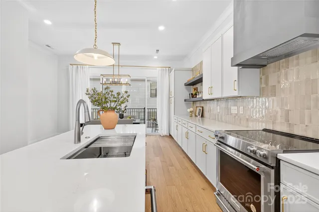 a large kitchen with stainless steel appliances granite countertop a stove a sink a refrigerator white cabinets and wooden floor