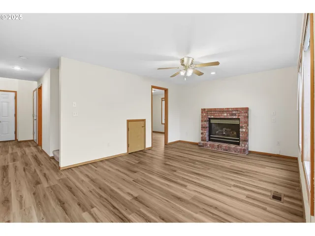a view of an empty room with wooden floor fireplace and a window